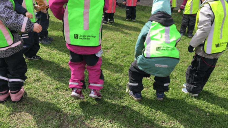 Barn i reflexvästar står i grupp på en gräsmatta och förbereder sig för en aktivitet.