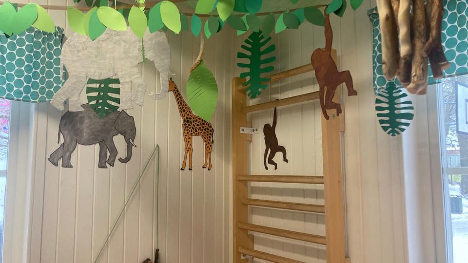 Pappersdjur som elefant, giraff och apor hänger från taket ovanför en ribbstol i ett lekrum.