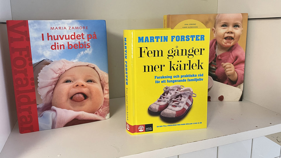 Böcker om småbarn och familjeliv uppställda på hylla, foto.