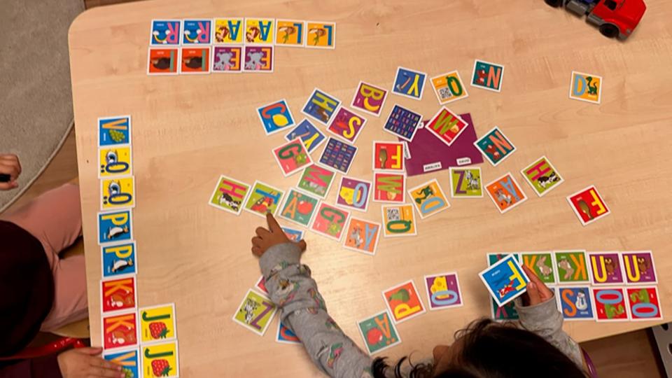 Tre barn sitter vid ett bord och spelar ett bokstavsspel.