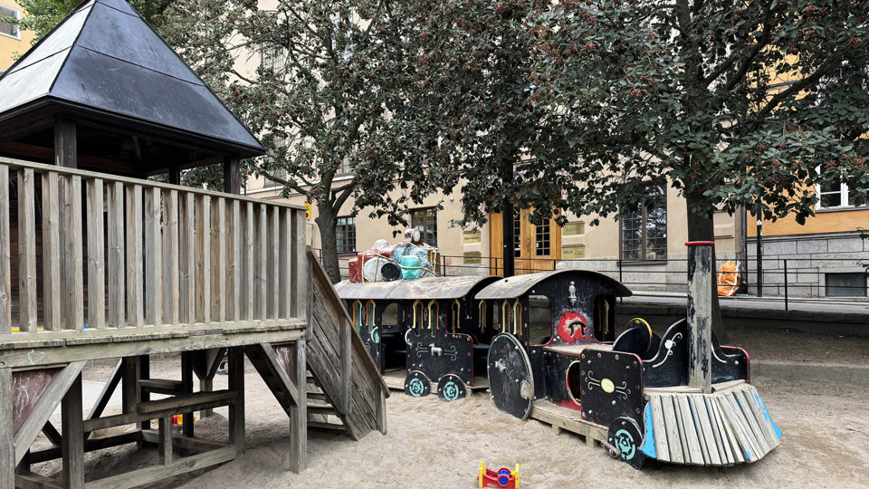 En lekpark med lekredskap i form av ett tåg och ett hus.