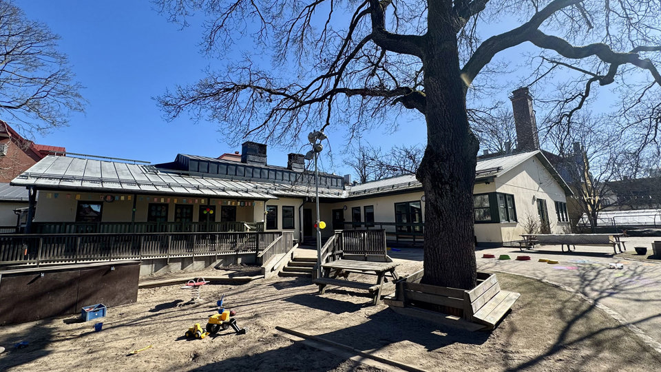 Solbelyst gård utanför förskola. Sandlåda i förgrund, foto.