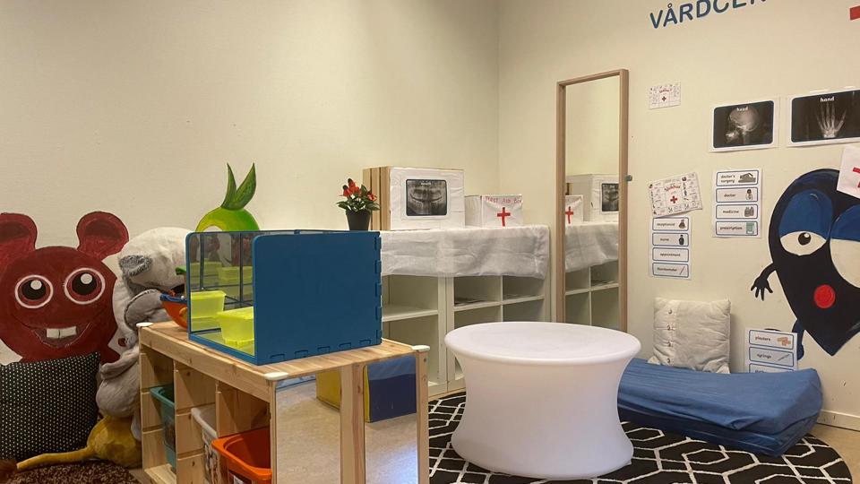 En lekhörna med doktorssaker och texten vårdcentral skriven på väggen.