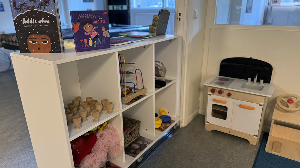 En lekhörna med en leksakspis och hyllor med leksaker och böcker.