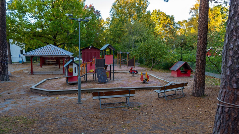 Skuggig lekplats omgiven av träd, foto.