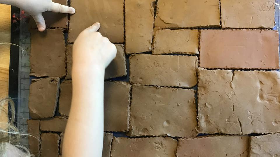 Barn bygger en mur av lerklossar på en arbetsyta.