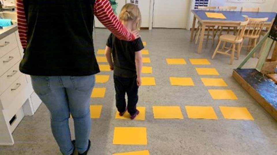 barn och pedagog som går på gula markeringar i golvet
