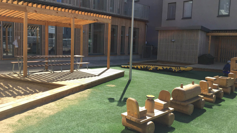 Utemiljö med lekytor, bord under tak och leksakståg i trä.