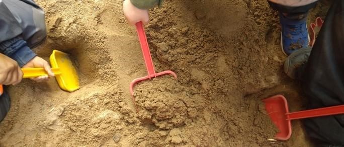 Barn gräver med spadar i sand utomhus.