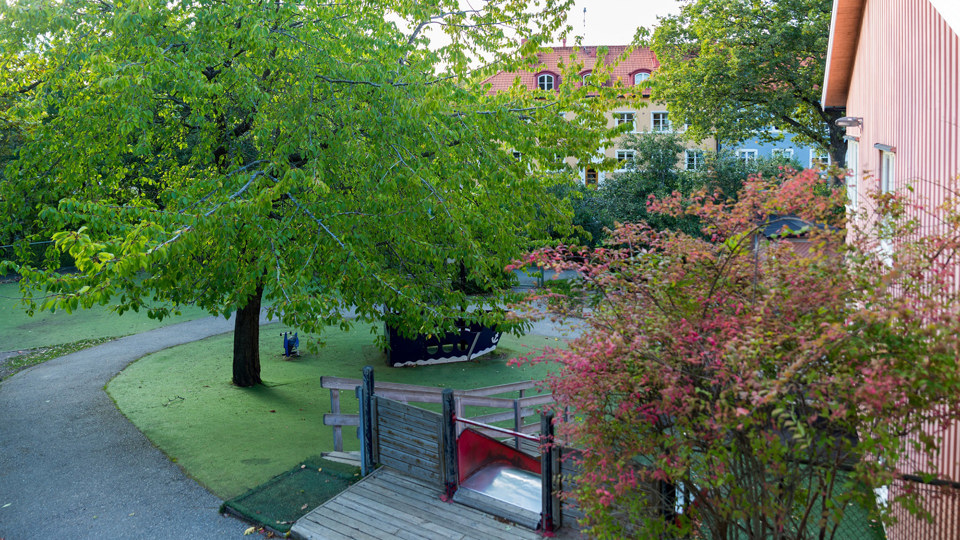 Grönskande förskolegård med rutschkana och andra lekredskap.