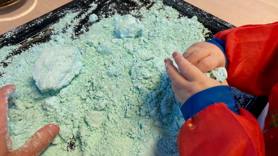 Ett barn leker med blågrönt pulver på en bricka.
