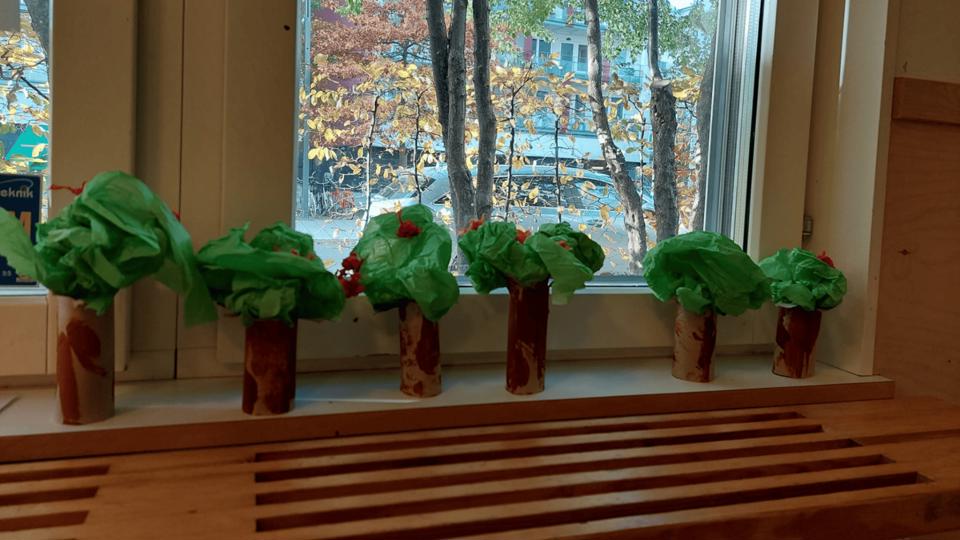 Fem pappersrullar med gröna blad som ser ut som träd, placerade på ett fönsterbräde.