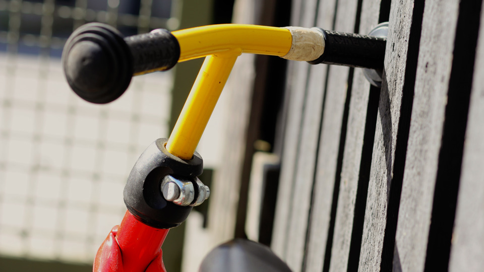 Cykelstyre i gult med svarta handtag står lutad mot en träpanel.