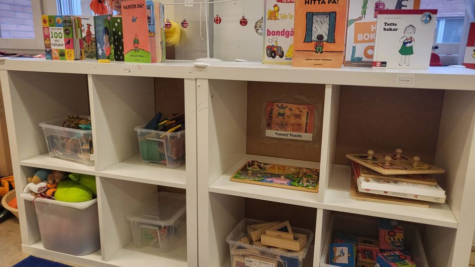 En bokhylla fylld med spel och platsbackar med leksaker och små böcker i. 