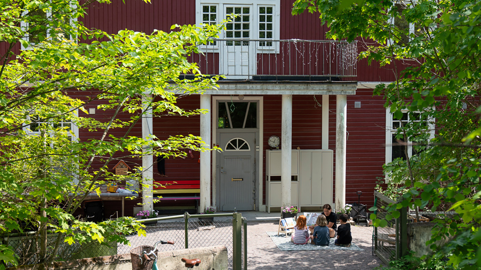 En husentré och en grupp barn som sitter utanför på en filt.