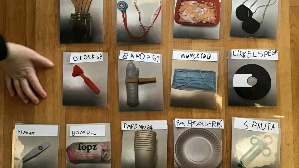 Kort med bilder på sjukvårdssaker, till exempel plåster, spruta, munskydd och stetoskop, uppställda på ett bord.