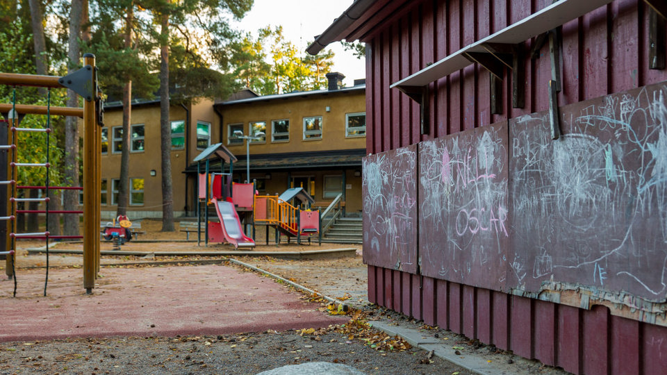 Avståndsbild beigebrun byggnad med lekplats i förgrunden, foto.