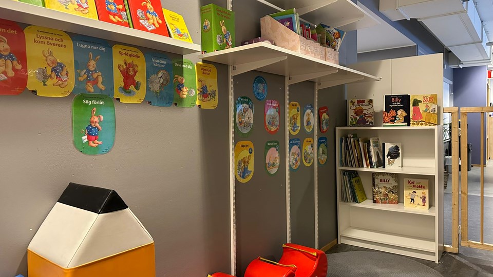 En vägg med hyllor med barnböcker. På golvet finns det sittkuddar.