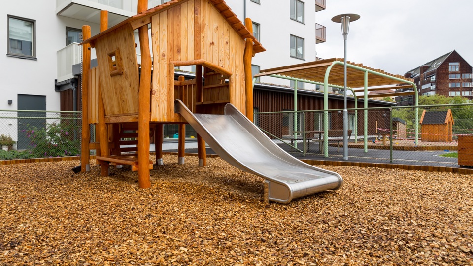 Del av innergård till flerbostadshus med ett klätterhus med rutschkana.