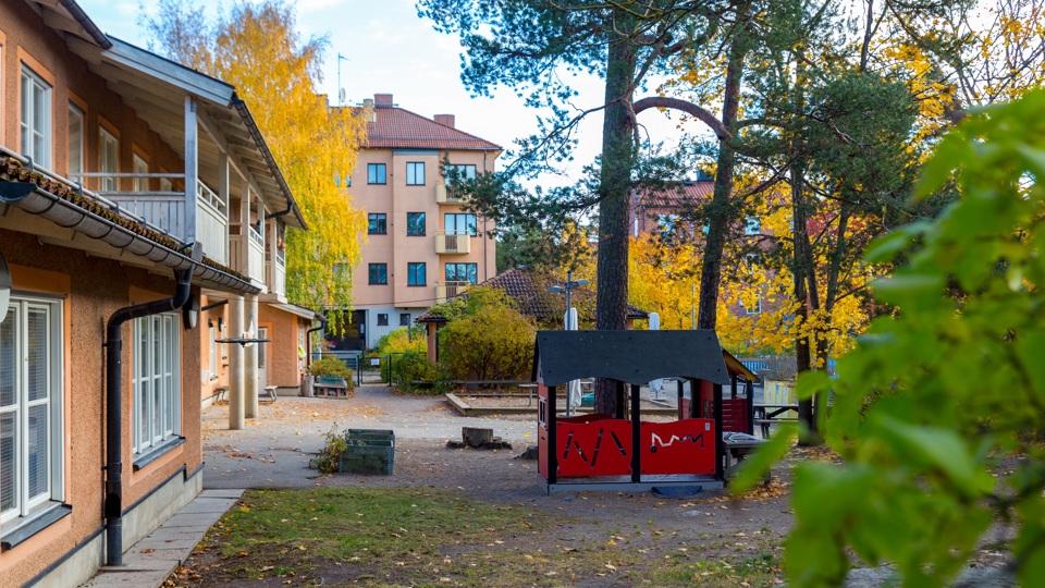 Gård med lekhus och träd framför en byggnad