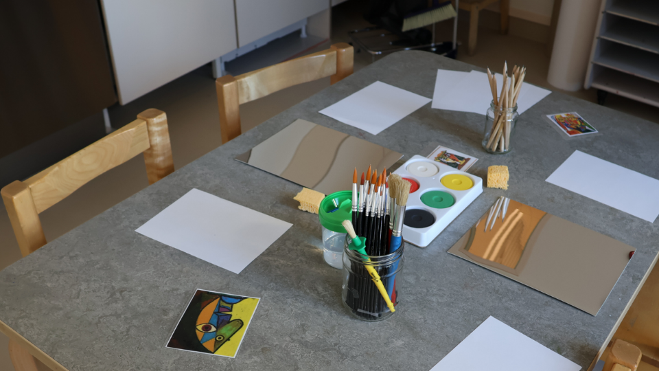 Ett litet bord med stolar, anpassade för barn. På bordet finns papper och vattenfärger samt en bild på ett konstverk av Picasso. Foto.