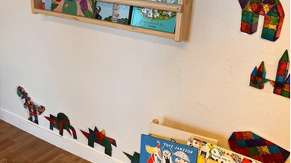 En vägg i förskolan med planscher och bokhyllor med böcker.