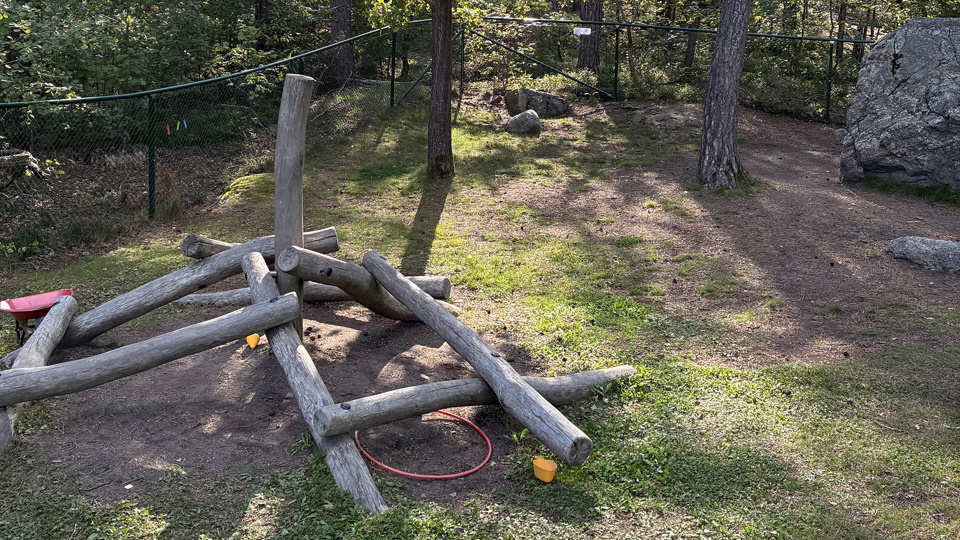 Klätterredskap i trä omgivet av träd och gräsmatta