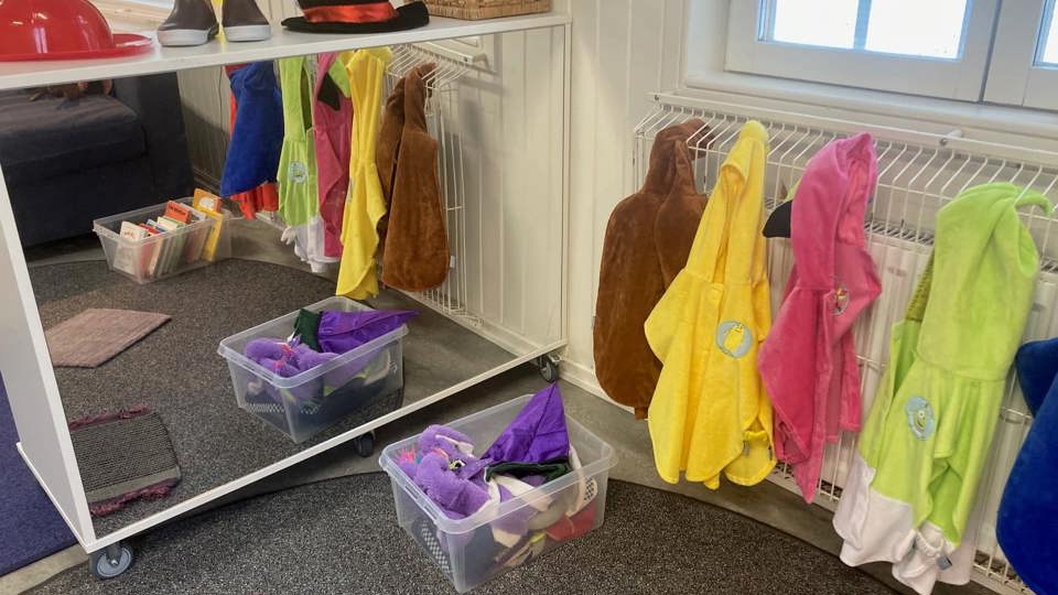 Klädhörna på en förskola med färgglada utklädningskläder, hattar och stövlar på ställningar och i lådor.