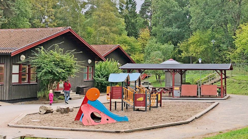 Förskolegård med rutschkana, sandlåda och andra lekmöbler.