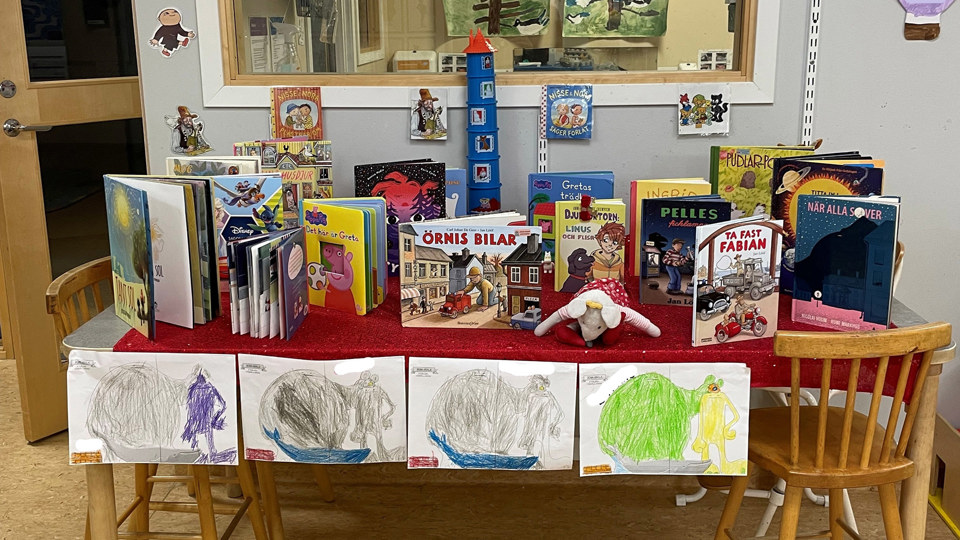 Ett bord fyllt med böcker, leksaker och teckningar.