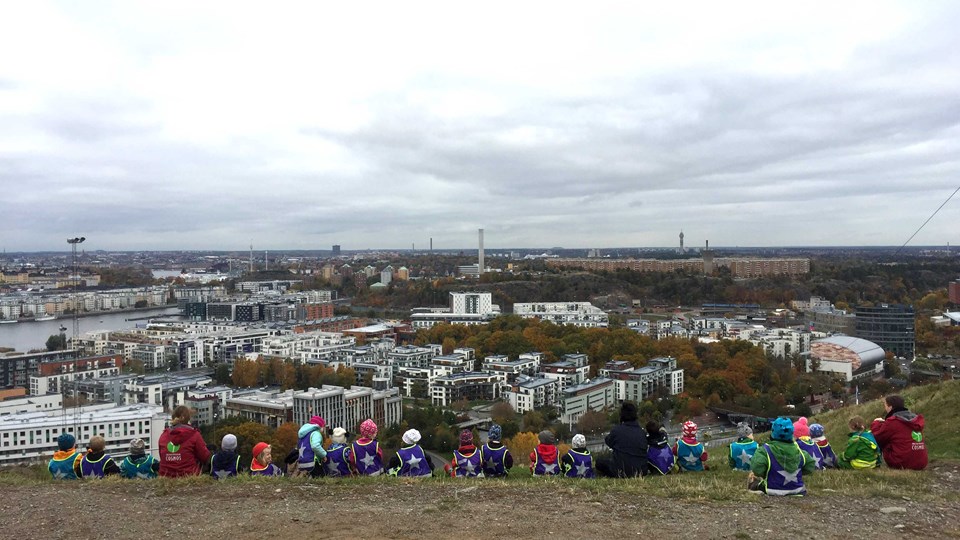 Barn och pedagoger sitter på ett berg och tittar på utsikten