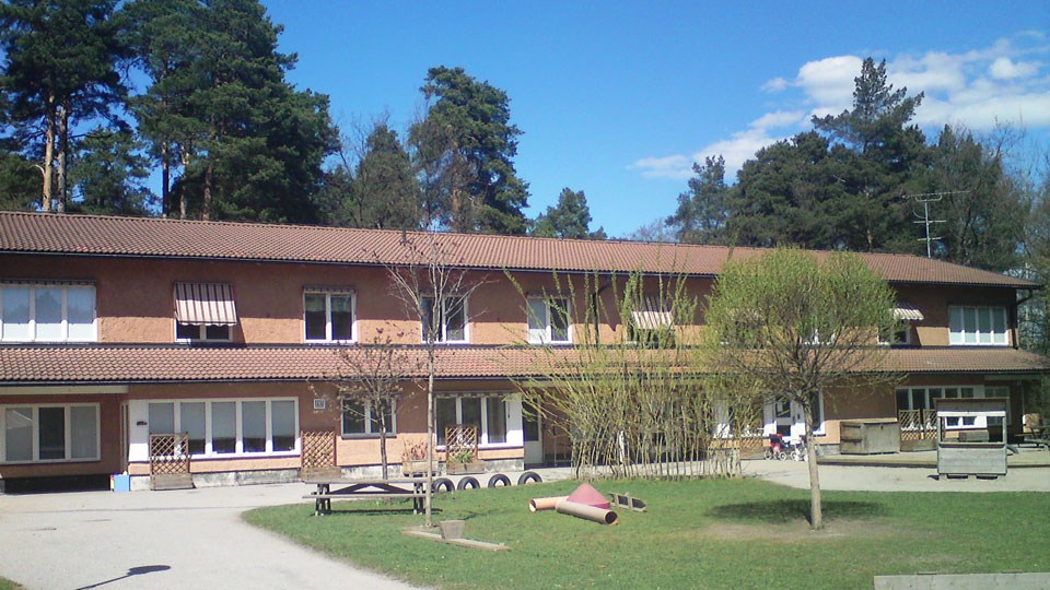 Årstalidens gård med förskolan i bakgrunden. tvåvåningshus i rödbrun puts.