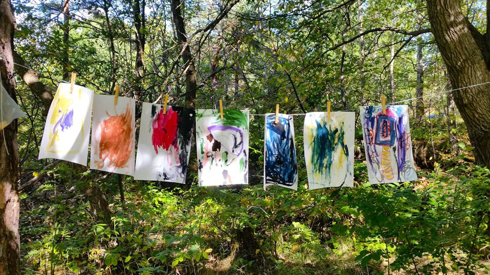 Teckningar upphängda med klädnypor på ett snöre i skogen.