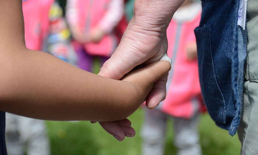 Barn och vuxen håller varandra i händerna runt midsommarstången på förskolan.