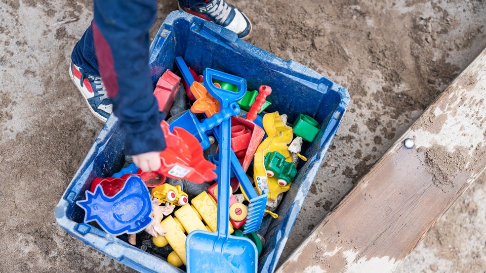 Barn som tar upp en leksak ur en låda som står i en sandlåda