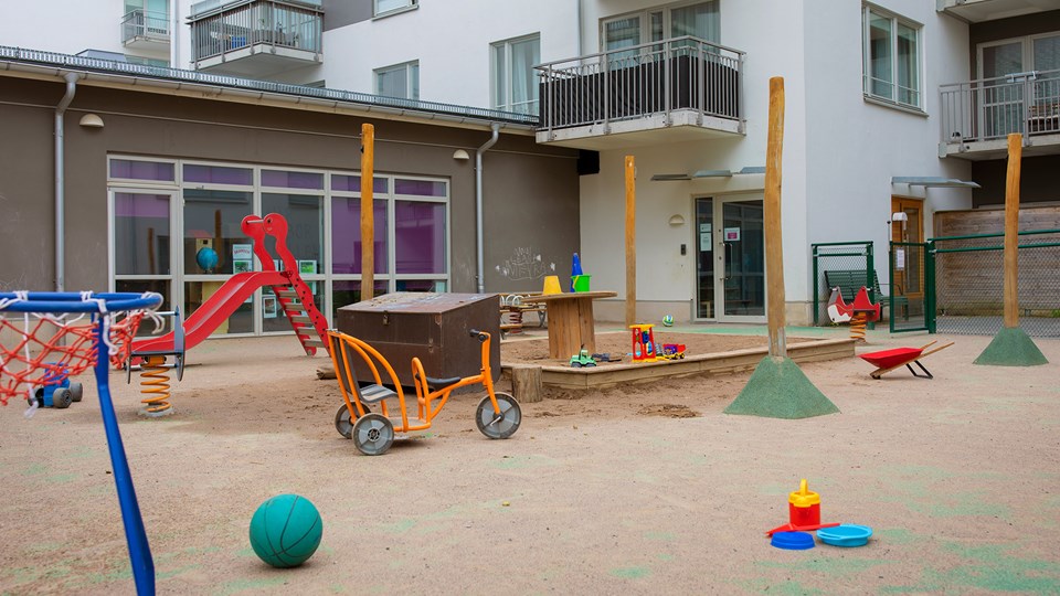 Förskola med stor sandlåda med leksaker i. I övrigt asfalt med trehjulingar, rutschkana, basketboll och andra leksaker.