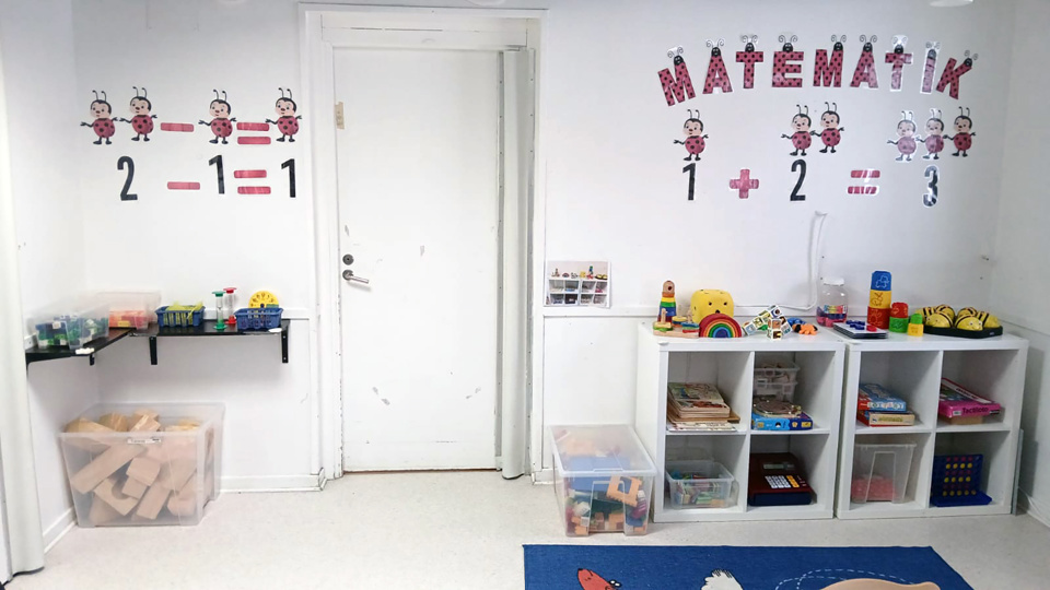 Ett rum med hyllor fyllda med leksaker och spel. På väggen står ordet "Matematik" och siffror och nyckelpigor.