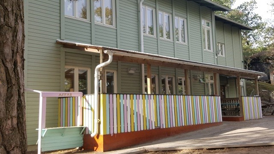 Ljusgrön tvåplansbyggnad med staket målad i olika färger.