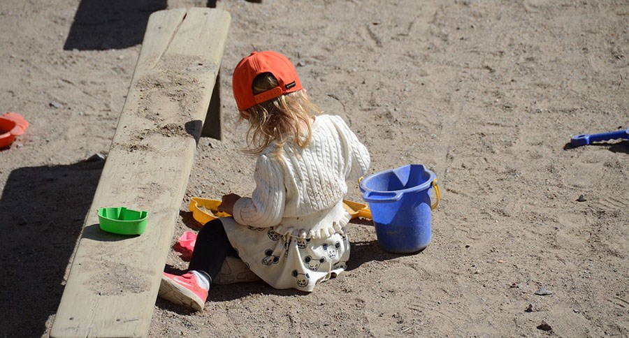 Ett barn leker i sandlådan med leksaker på förskolans utegård.