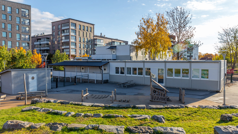 Gräsmatta med stora stenar på framför förskola. Vid sidan om förskolan finns höghus.