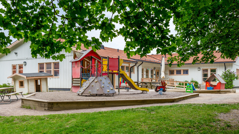 Grönskande utegård med klätterställning framför förskola.