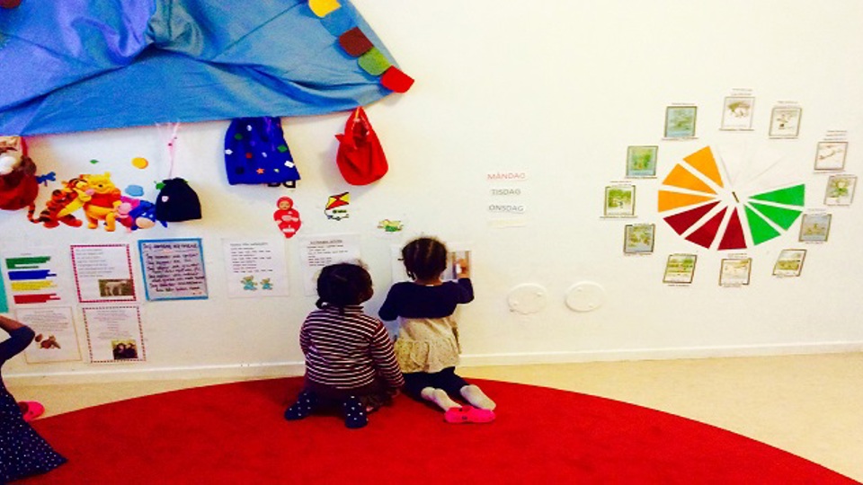 Två barn sitter och tittar på texter och bilder som är uppsatta på en vägg.