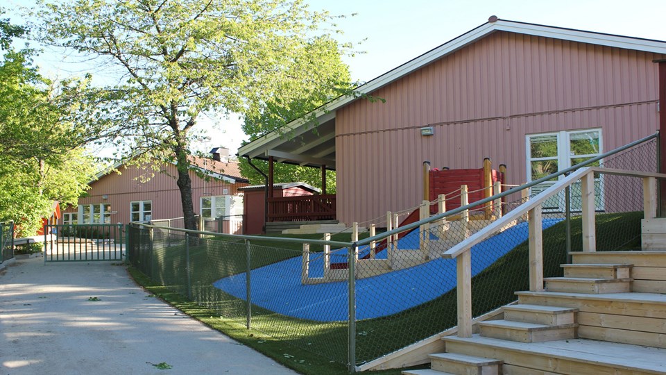 Förskolan Trollhöjdens rosa fasader och en del av förskolans gård med rutschkana och trappor.