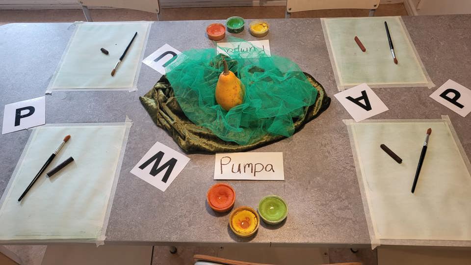 Förskolemiljö med kreativt pysselbord, barnböcker, växter och material ordnade på hyllor.