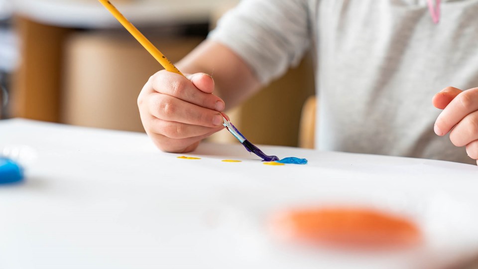 Barn sitter med en pensel i handen och målar