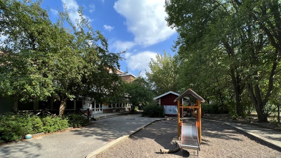 En förskolegård med en sandlåda och en liten rutschkana.