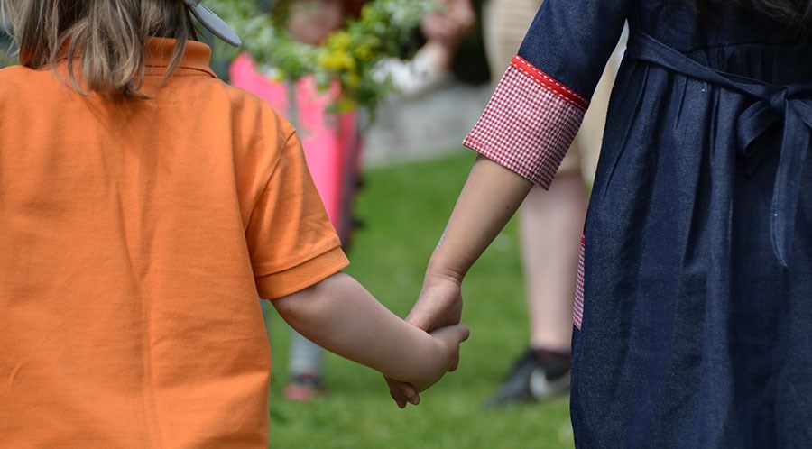Barn håller händerna i en cirkel runt midsommarstången på förskolan.