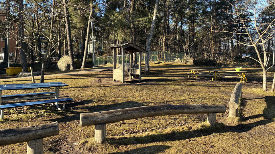 En förskolegård med lekytor och lekredskap i trä. Sittplatser och stockar att balansera på.