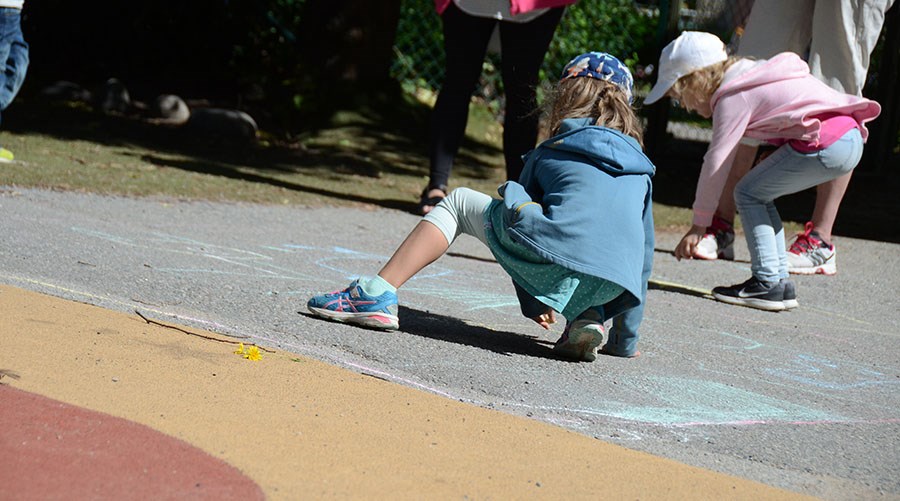 Barn målar med kritor på asfalten ute på förskolans gård.
