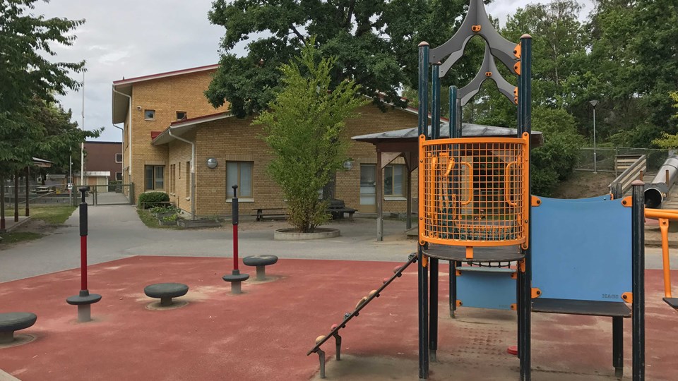 Foto på utegården med förskolans tegelfasad i bakgrunden och lekutrustning.